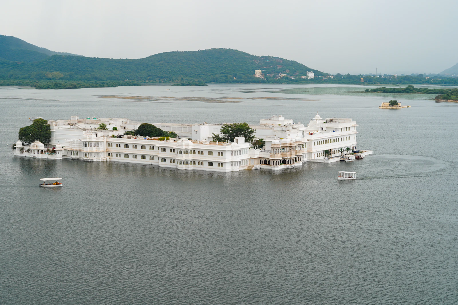 The white marble Taj Lake Palace sitting on an island in Lake Pichola, Udaipur, with hills behind
